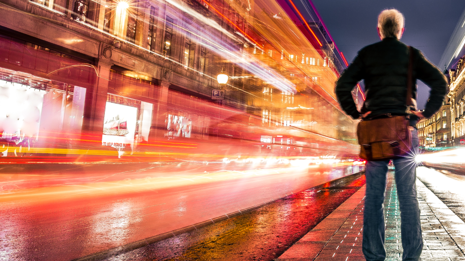 A light-filled image of a person standing on a rain-soaked street.