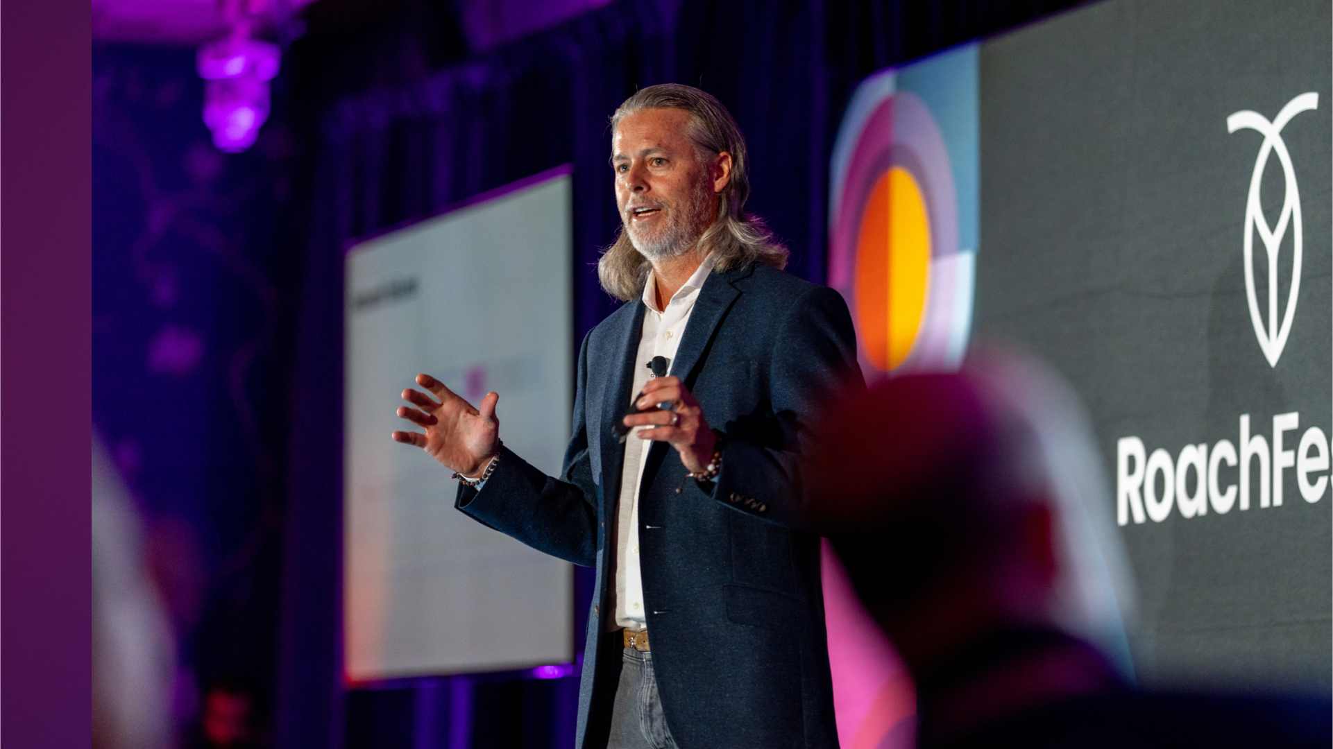 Spencer Kimball, CEO and Co-Founder of Cockroach Labs, presents on stage at RoachFest Las Vegas 2025 about the distributed SQL database CockroachDB, standing before a large screen displaying the Cockroach Labs logo and event visuals in purple and orange lighting.